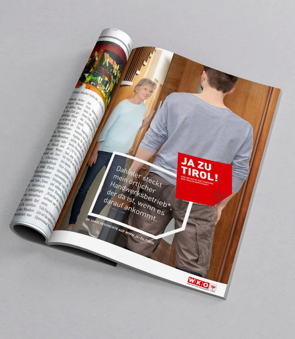 Aufgeschlagenes Magazin mit Werbeanzeige der JA ZU TIROL! Kampagne. Auf dem Bild steht eine ältere Dame in hellblauem Oberteil lächelnd in einer Tür und begrüßt einen Handwerker von hinten gesehen. Im Vordergrund rotes Kampagnenlogo mit dem Text: Dahinter steckt mein örtlicher Handwerksbetrieb*, der da ist, wenn es darauf ankommt.